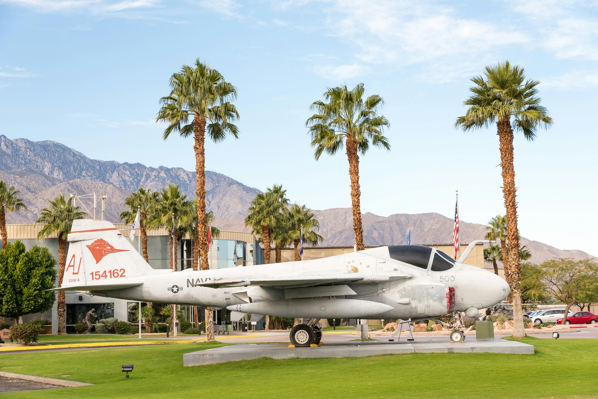 A small airplane standing in front of a museum building. Tall palm trees rise above it