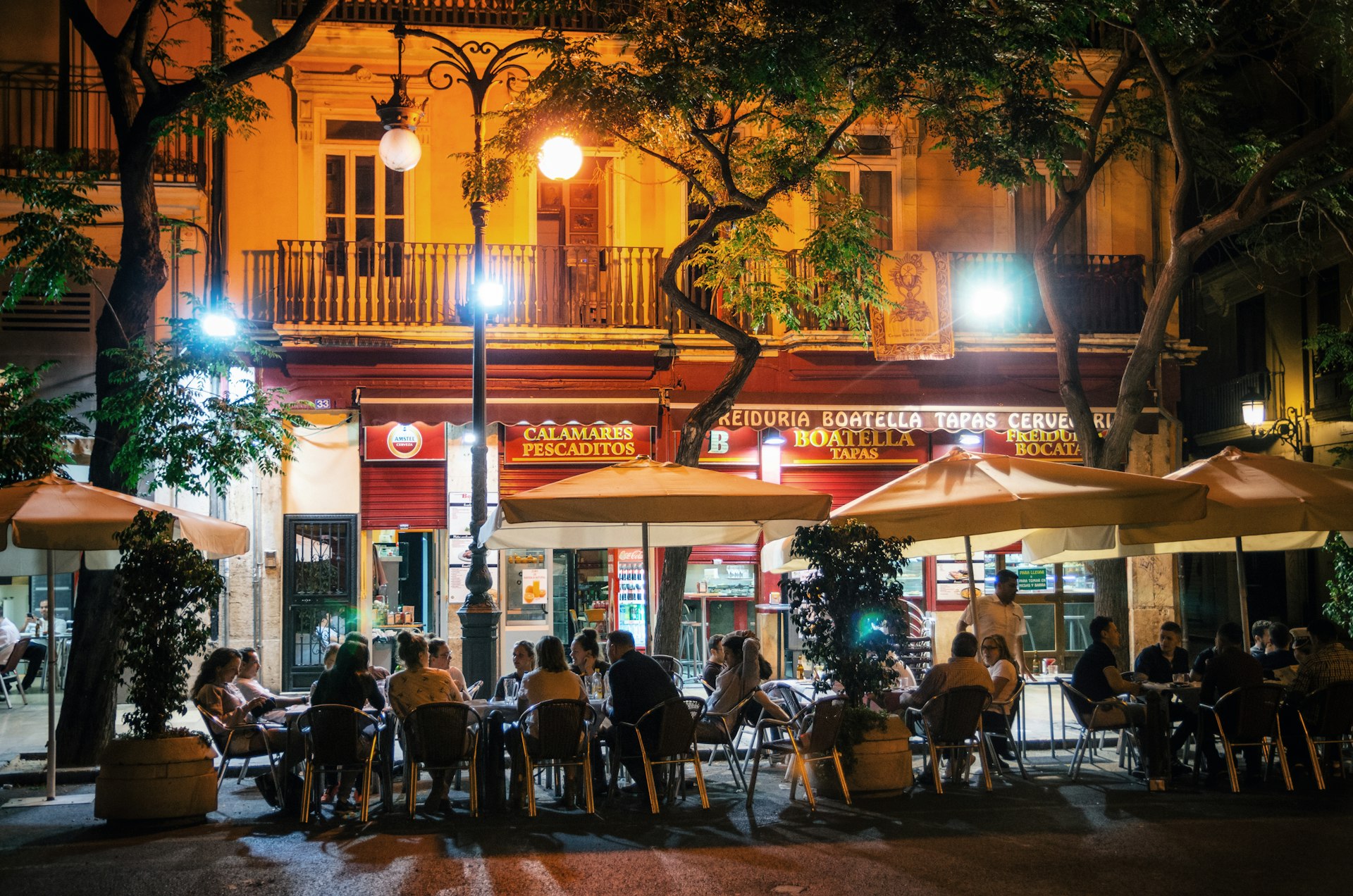 People sit outside a bar at tables and chairs in the evening