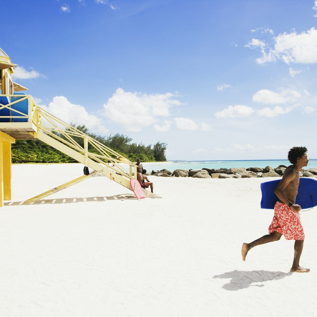 A bodyboarder runs along a beach in Barbados in front of a lifeguard tower
