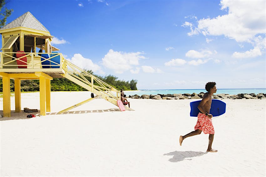 A bodyboarder runs along a beach in Barbados in front of a lifeguard tower