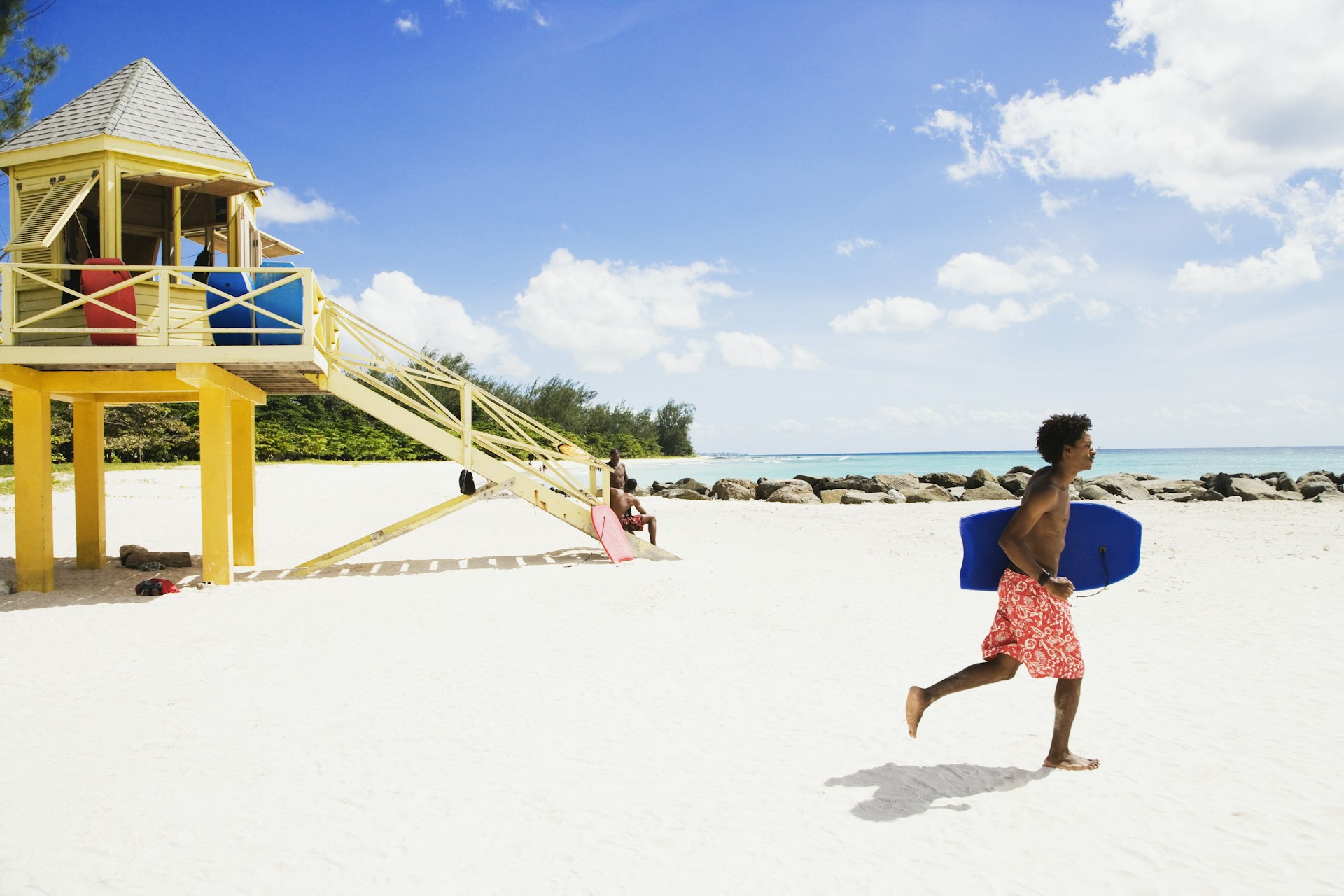 Young man runs with body board on beach.