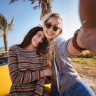 Two women pose in front of palm trees and a yellow car in Cyprus