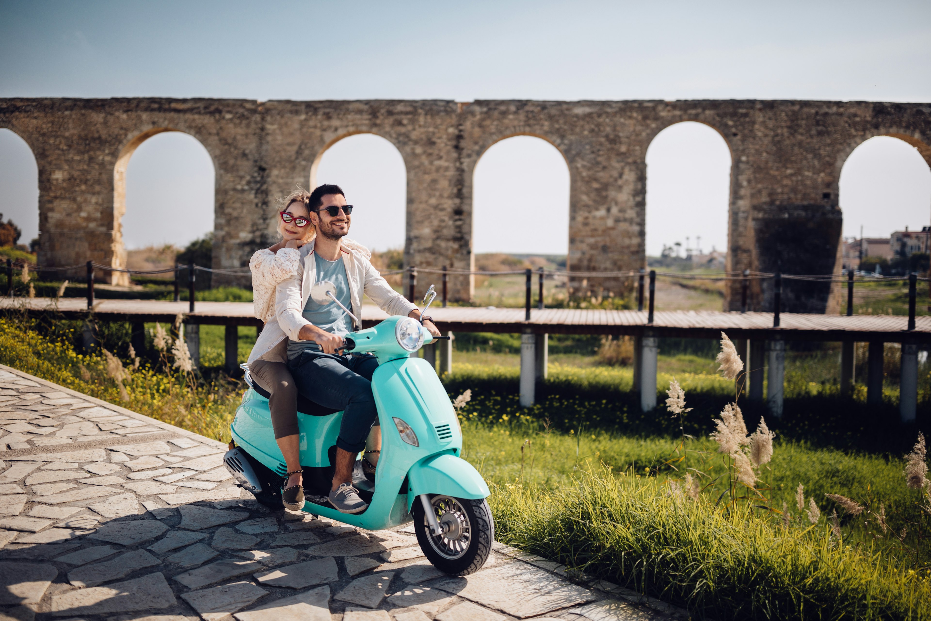 Young loving couple with vintage motorcycle riding next to ancient stone aqueduct monument in Cyprus