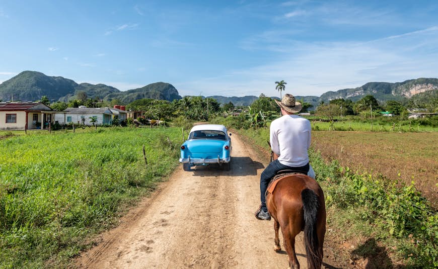 Classic car passes a man on horse in Vinales, Cuba
