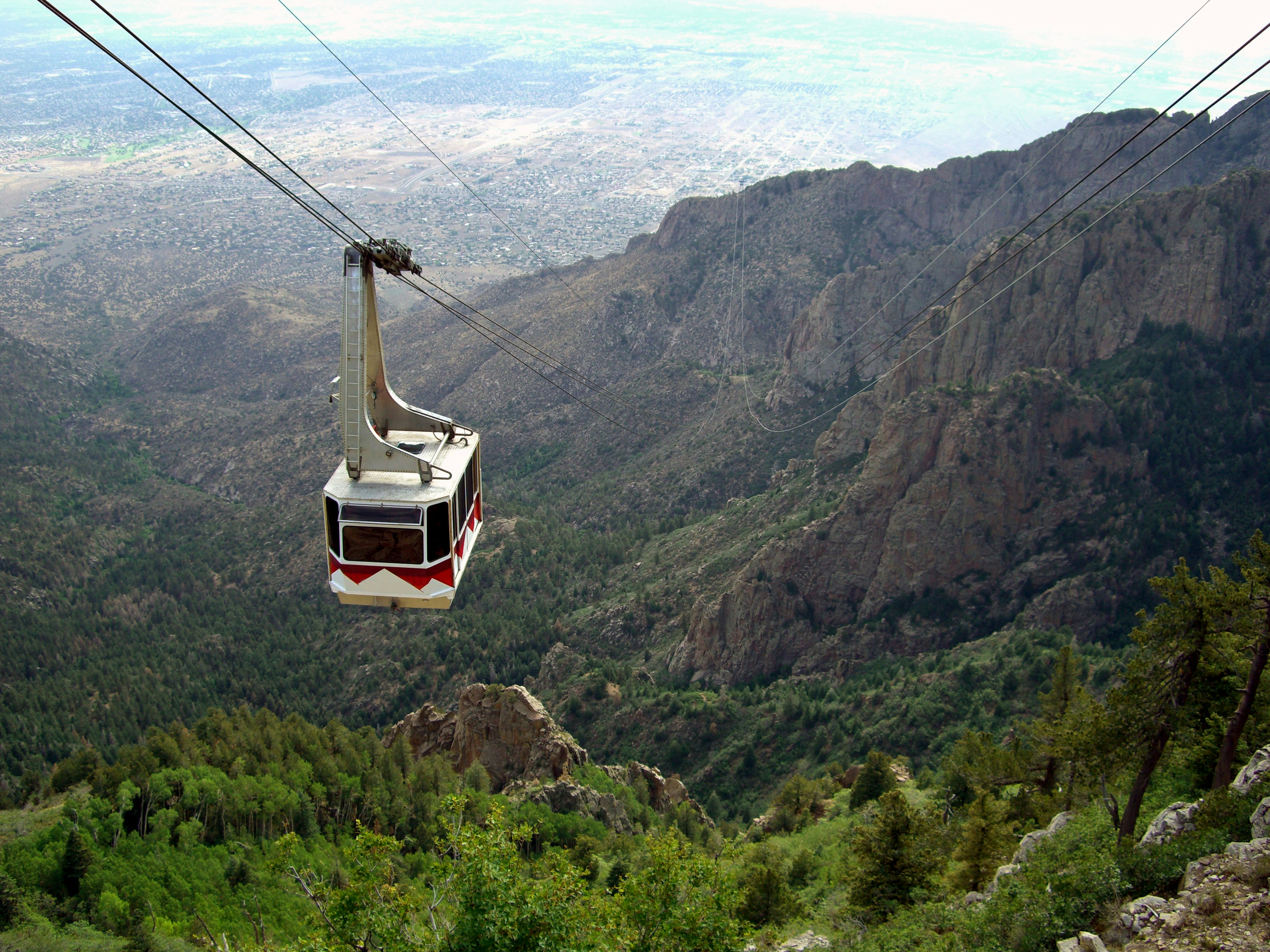 A cable car at the Sandia Peak Tramway approaching the top of Sandia Mountain, with the city of Albuquerque in the background.