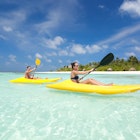 Couple kayaking in lagoon of tropical island near resort.