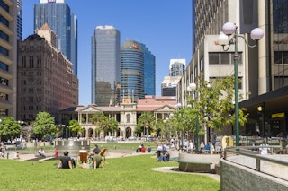 Brisbane, Australia - September 26, 2016: View of people sitting in lawn enjoying the sunshine in Post Office Square in Brisbane during lunchtime with skyline in the background.