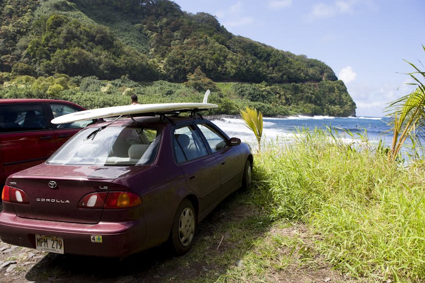 A red car parked at a beach with a surfboard on its roof