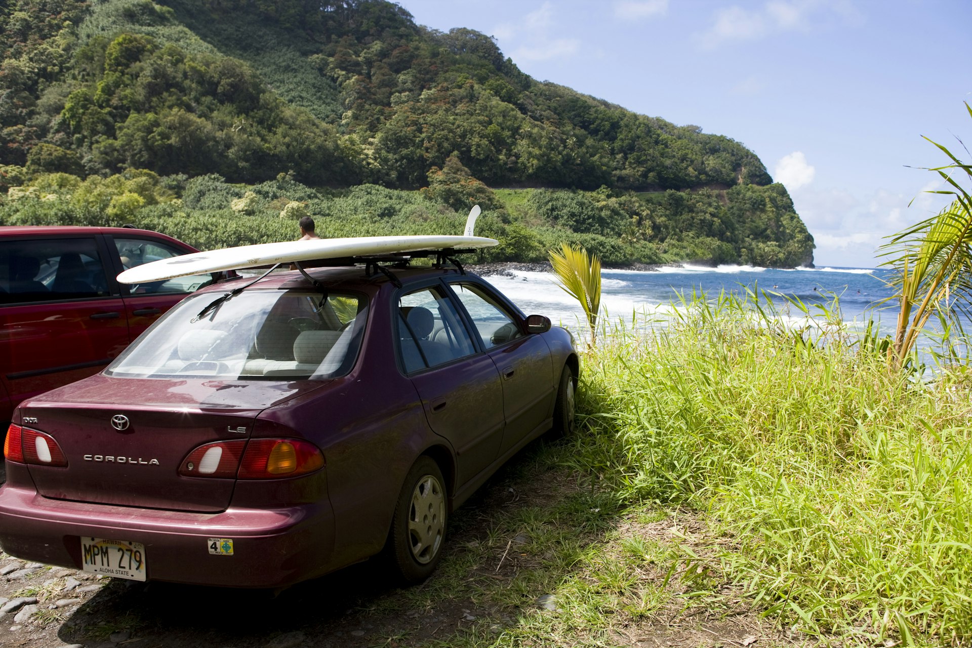 A red car parked at a beach with a surfboard on its roof