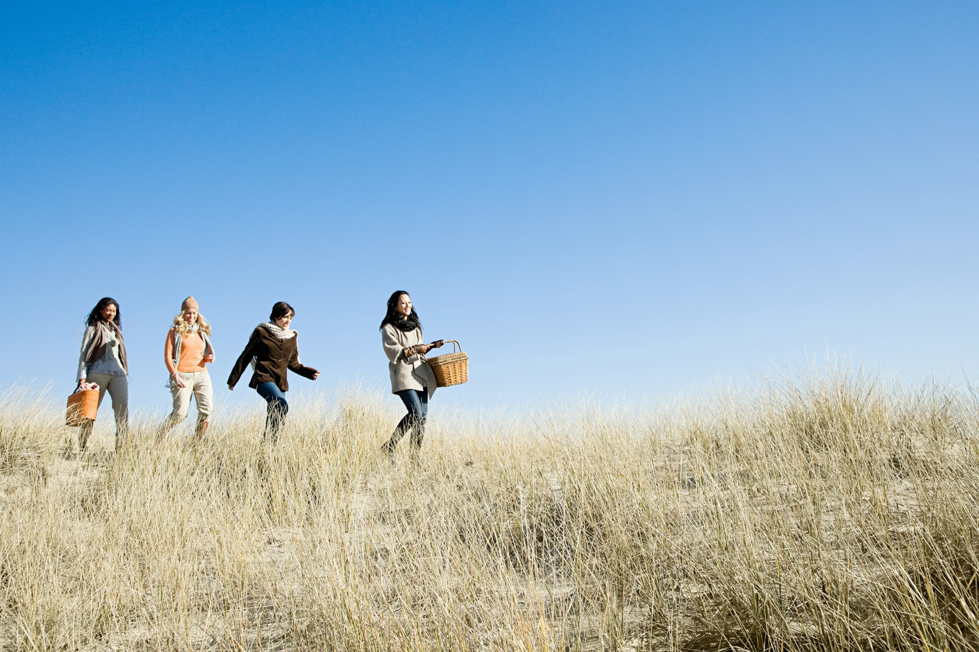 Female friends wearing coats and scarves, walking in marram grass on a sunny day in Cape Cod