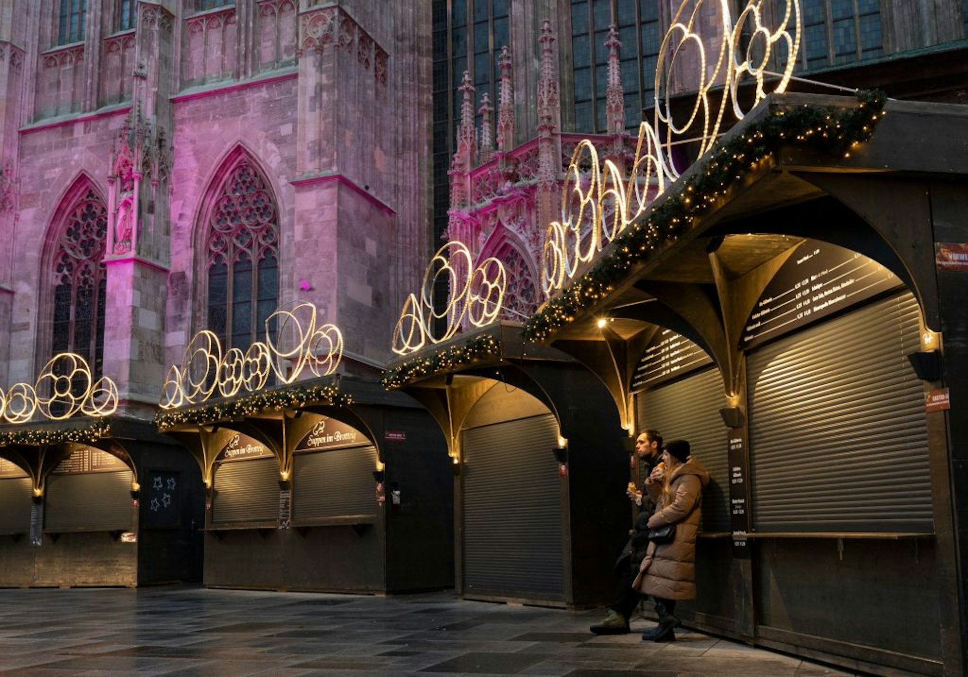 A couple eat a snack at the closed Christmas market next to Stephen's Cathedral in Vienna