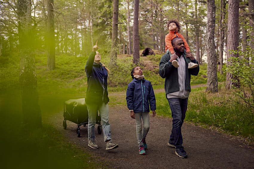 A woman points to the sky as she walks through the woods with her family