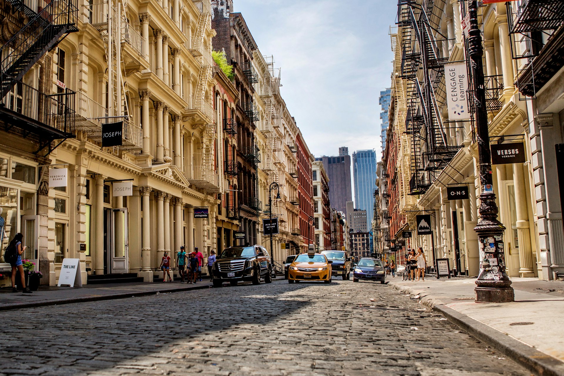 A cobblestone street in Soho with taxis, pedestrians and shops lining the sidewalks
