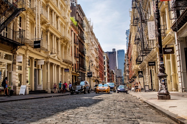 A cobblestone street in Soho with taxis, pedestrians and shops lining the sidewalks