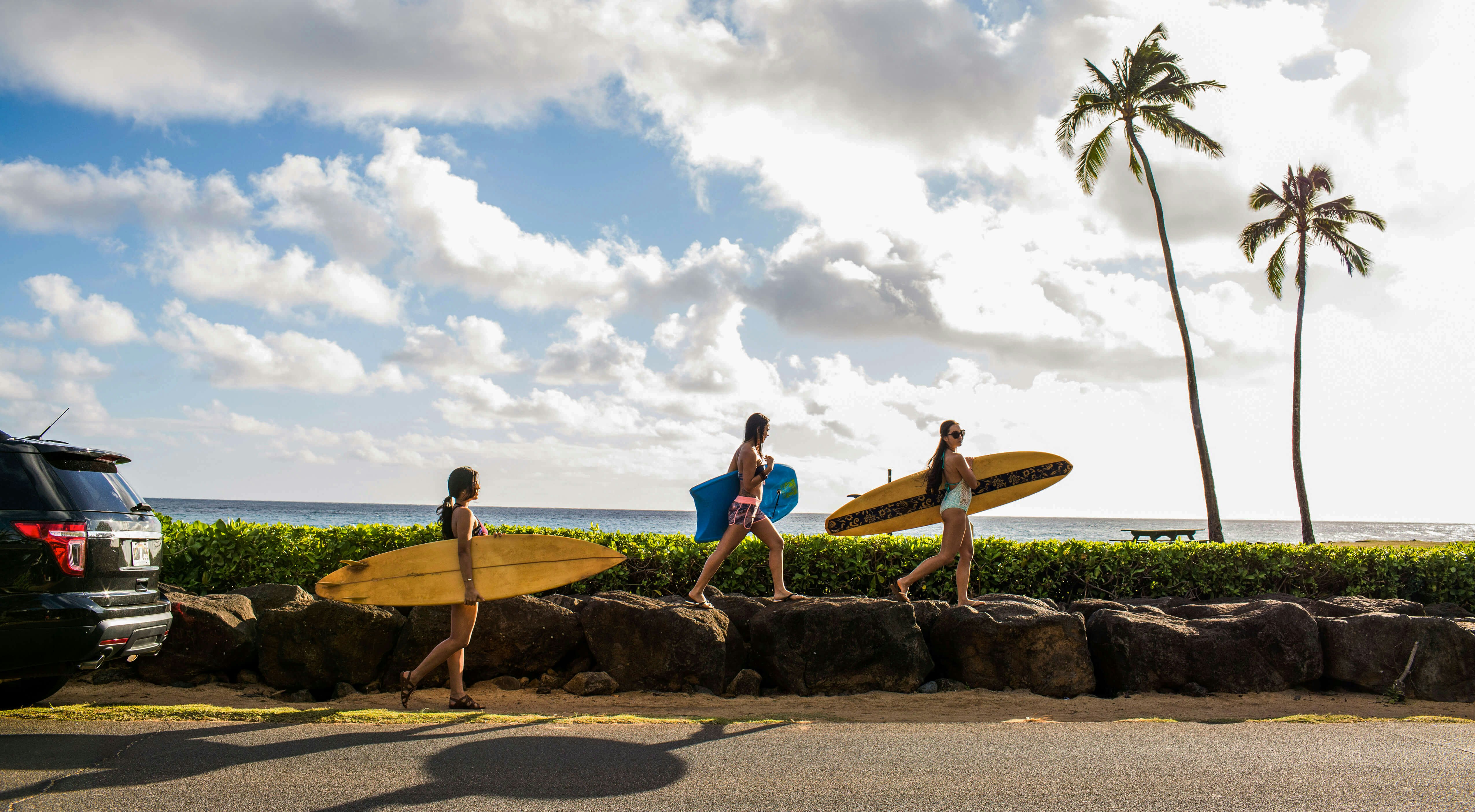 Three Pacific Islander surfers carrying their boards to the water