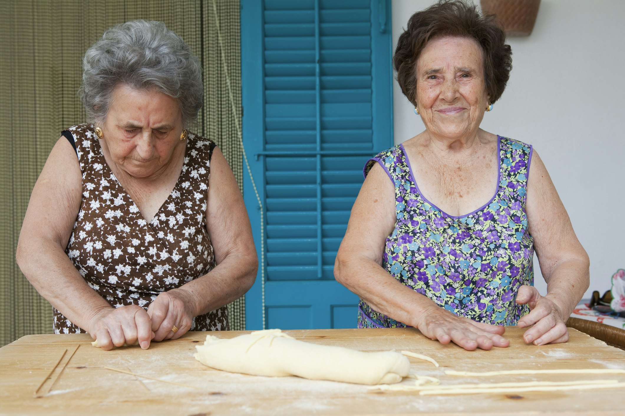 Two Sicilian women stand side by side making pasta together