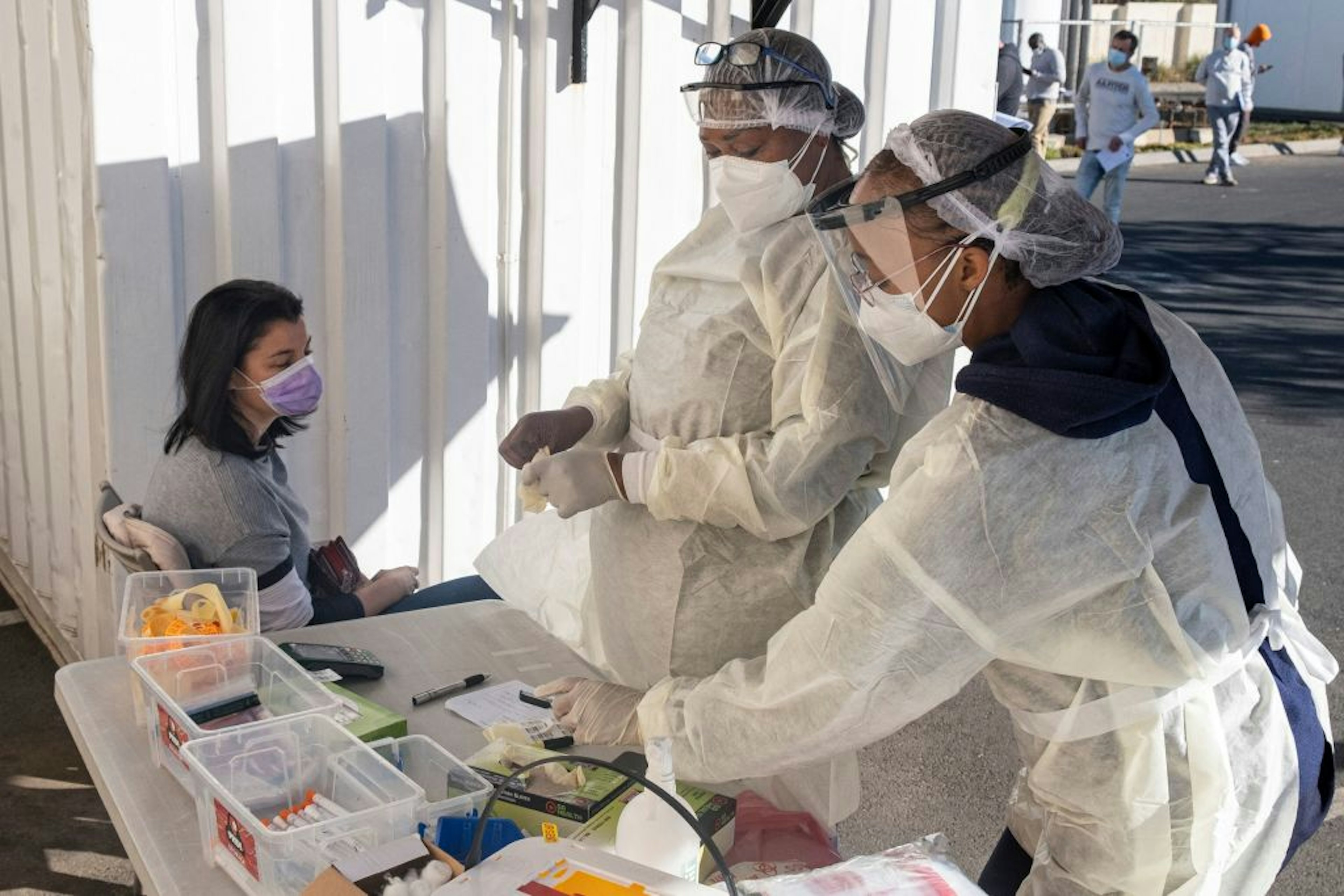 Health workers wearing personal protective equipment (PPE) prepare to test a woman for COVID-19