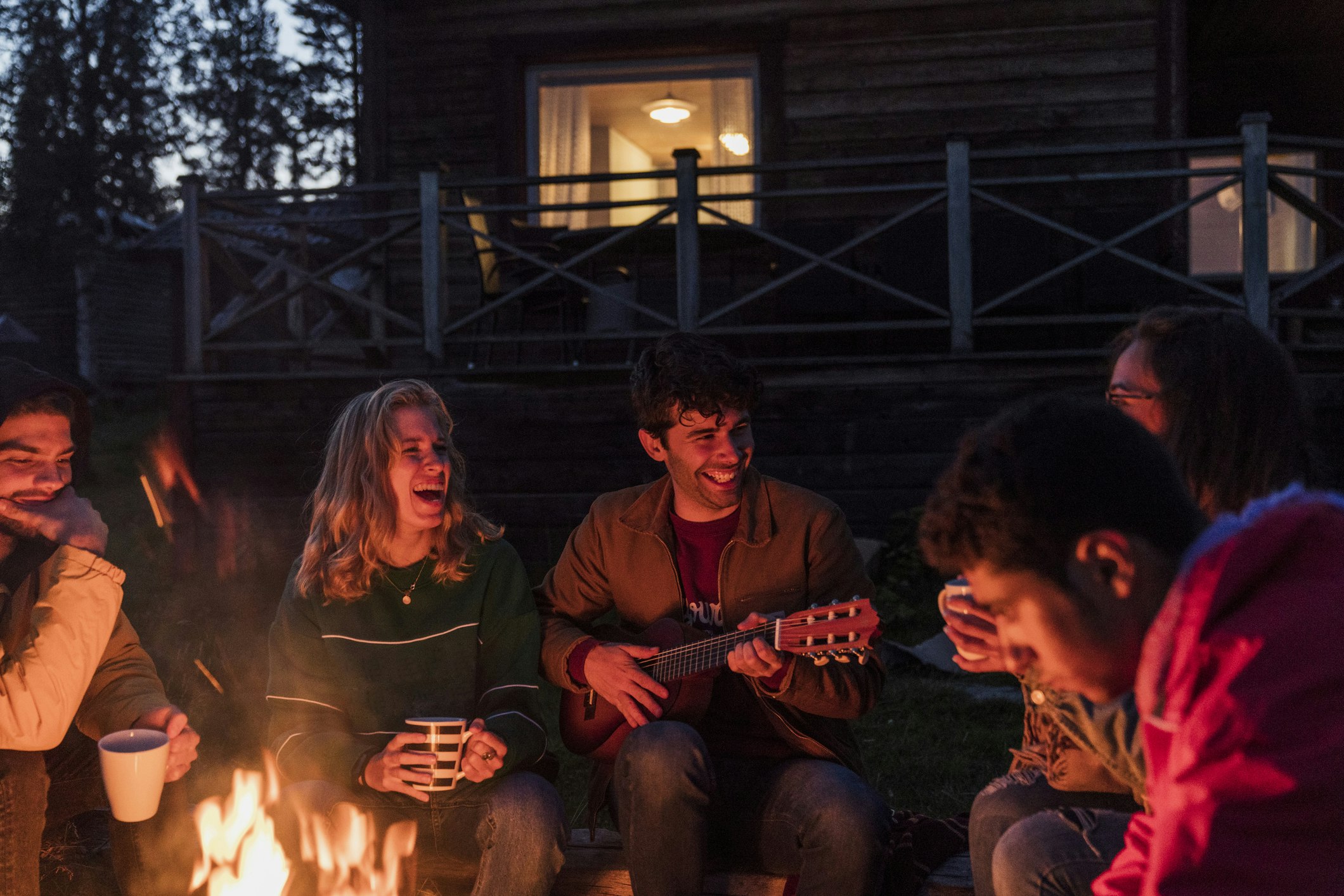 Group of friends sitting at a campfire, talking and playing guitar
