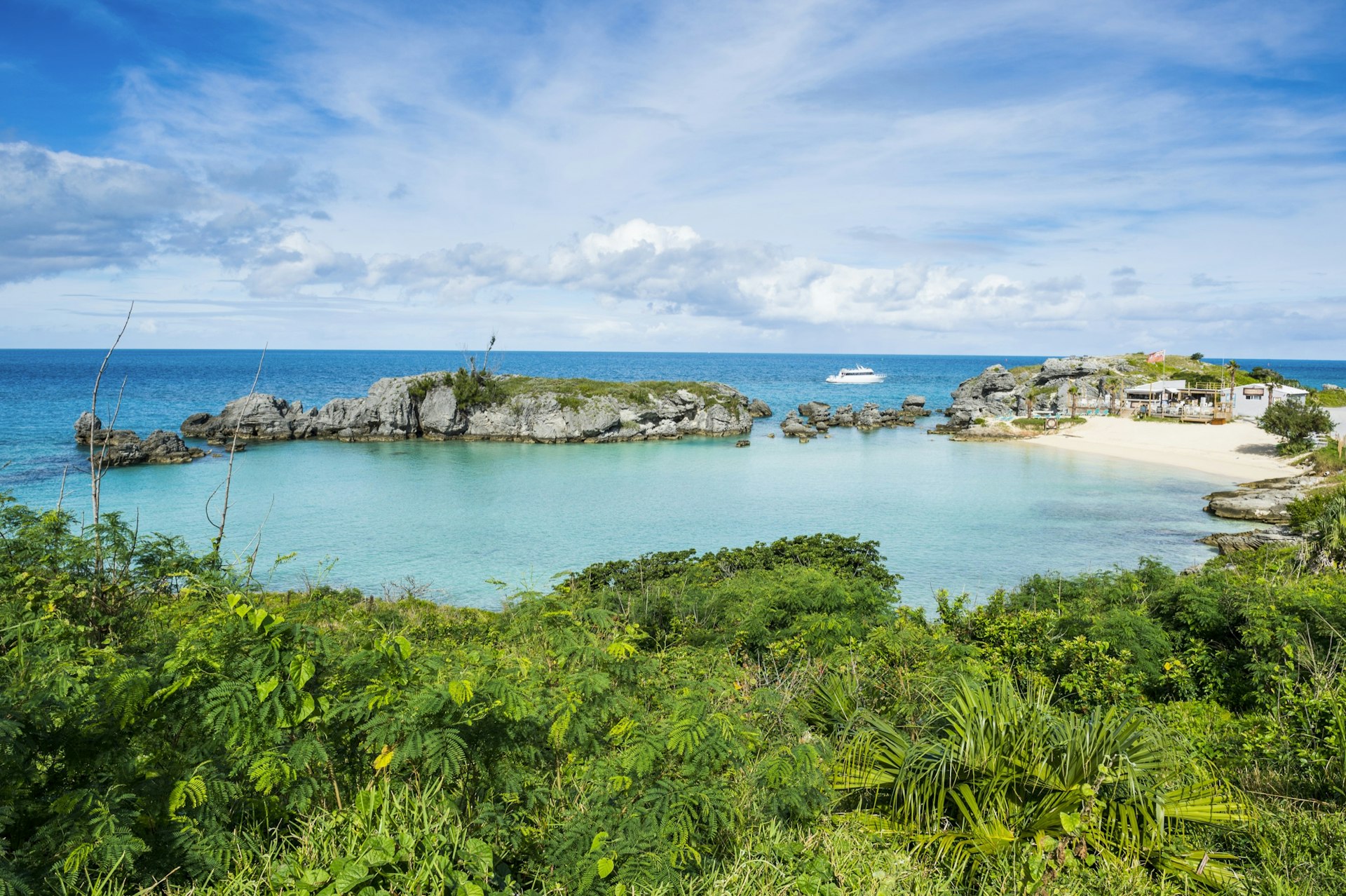 Bermuda's Tobacco Bay as seen from the greenery that surrounds this perfect white bowl of sand, with a white boat sailing past