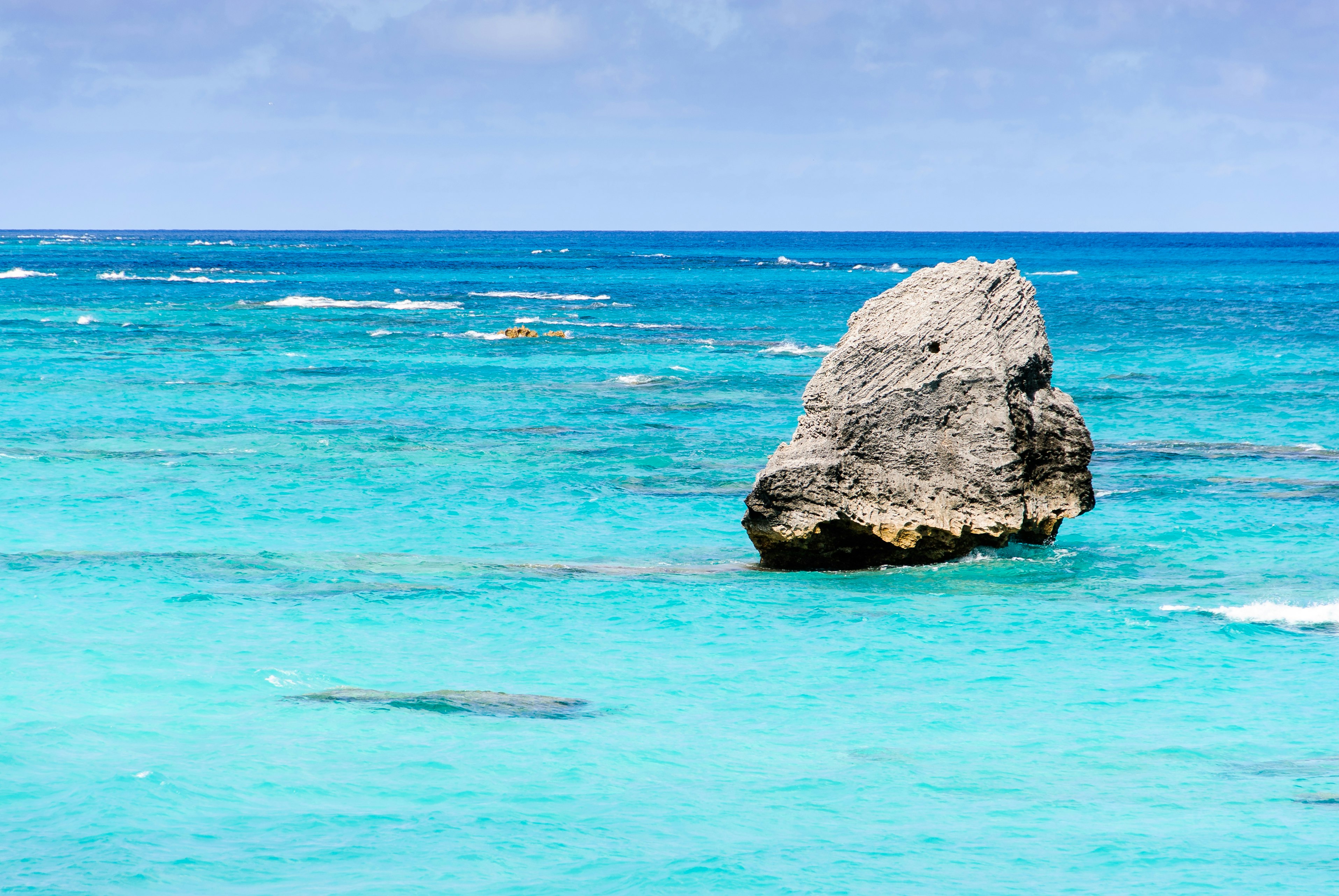 A large rock sticks out of the sea in front of Bermuda Warwick Long Bay Beach in Bermuda. 