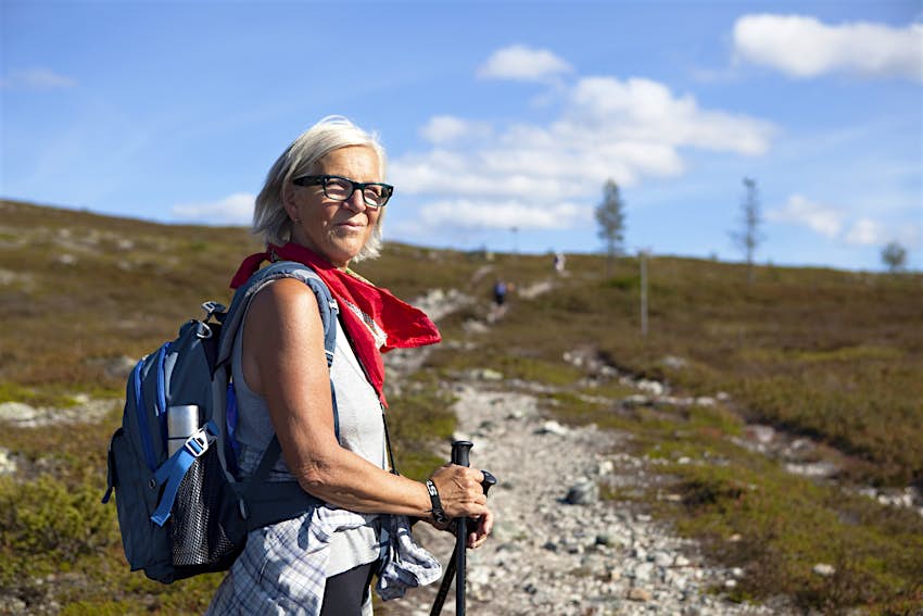 A woman walks up a hill in Dalarna and looks back at the camera