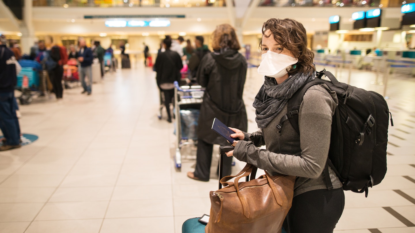 Woman waiting in a long line for a flight wearing a N95 face mask during a global pandemic