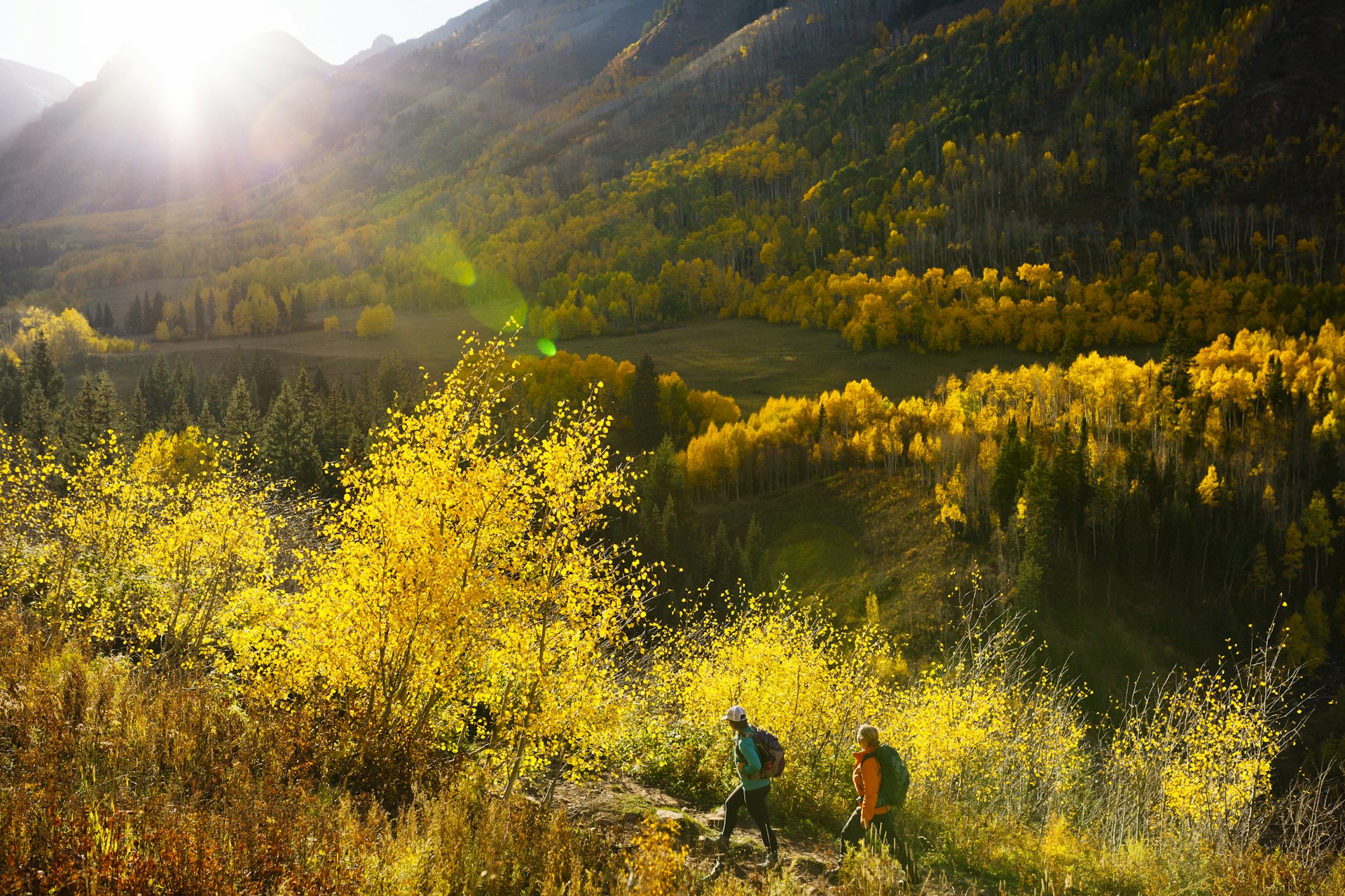 People hiking through mountainous fall foliage on a sunny fall day