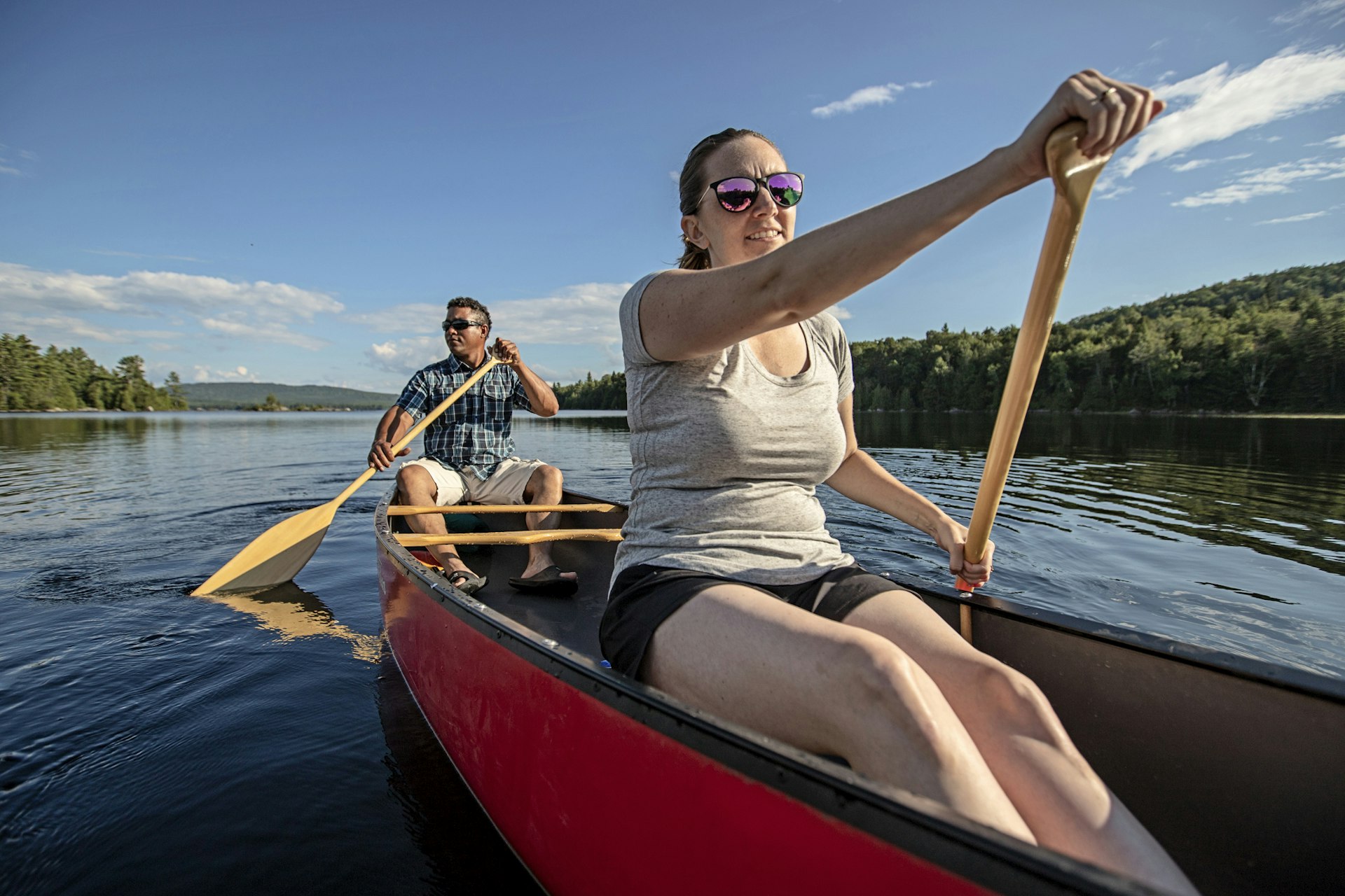 A woman and man steer a kayak on a woodland lake in Maine