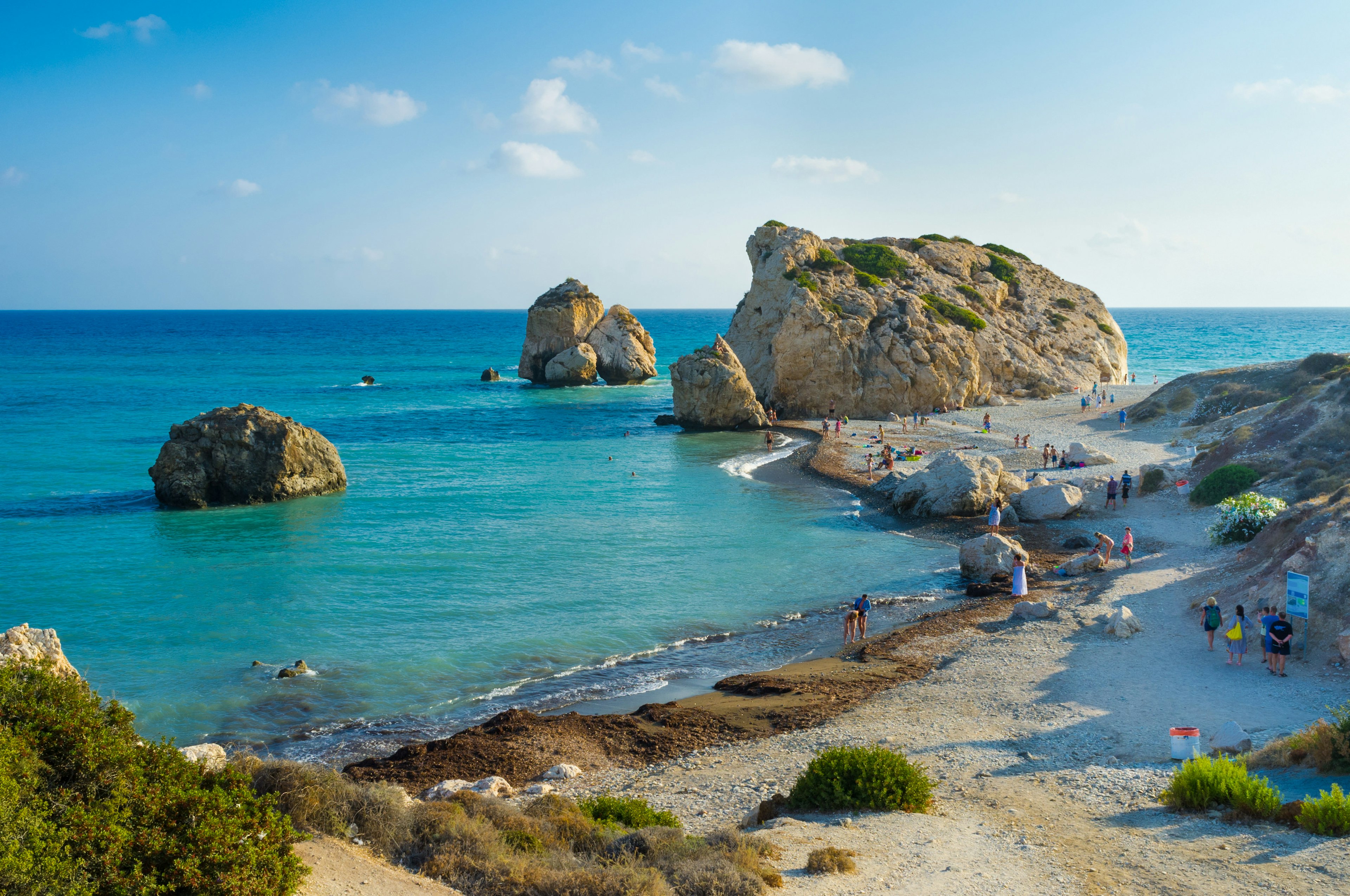 People walking on the beach as waves wash around Aphrodite's Rock