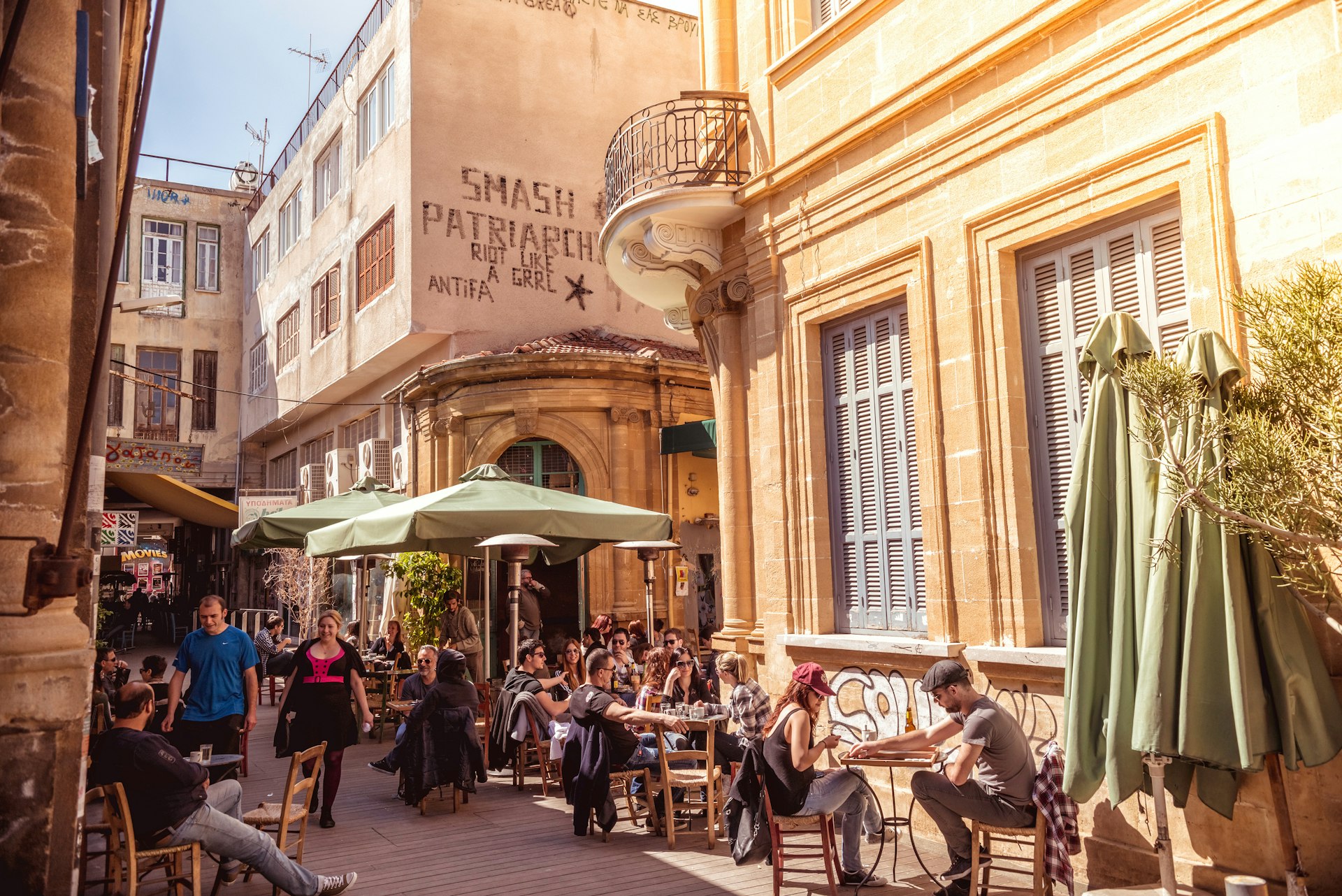 People in restaurants and coffee shops on Ledra street, lined with stone buildings, on a sunny day