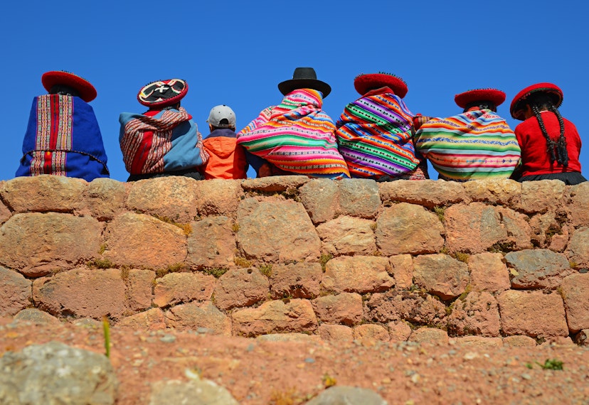 Quechua ladies and a young boy chatting on an ancient Inca wall, Peru.
