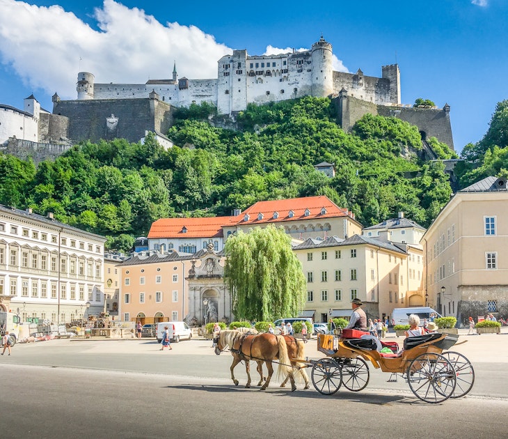 Beautiful panoramic view of the historic city of Salzburg with traditonal horse-drawn Fiaker carriage and famous Hohensalzburg Fortress on a hill on a sunny day with blue sky and clouds in summer; Shutterstock ID 1038459445; your: Claire Naylor; gl: 65050; netsuite: Online Editorial; full: Best places to visit Austria