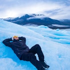 An Asian man resting on top of a glacier in Patagonia
