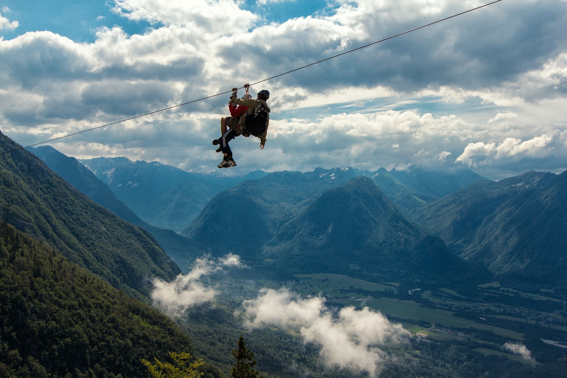 Two people sliding down a zip line with misty mountains behind them