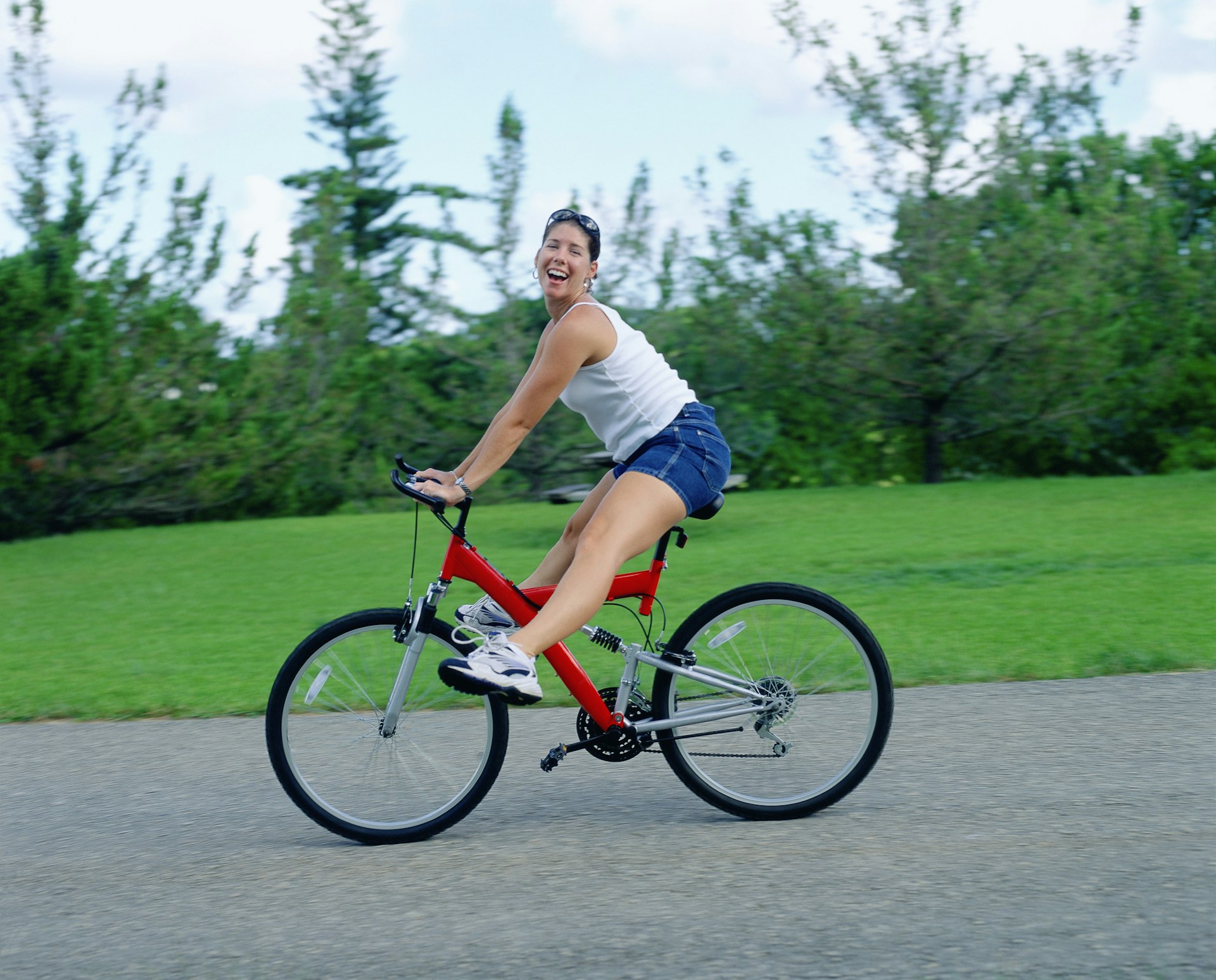 A young woman sticks both legs out and smiles at the camera as she rides a bike.