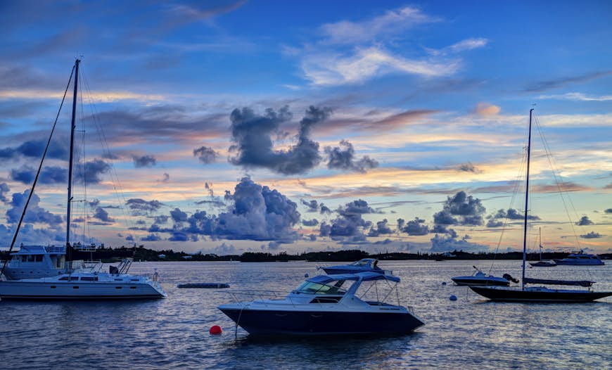 A trio of boats moored in the ocean during sunset. 
