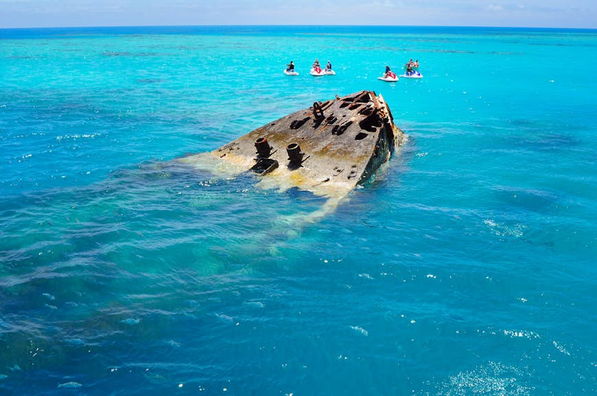 A group of people in jet skis stop next to a semi-submerged shipwreck in ocean near the Bermuda island. 