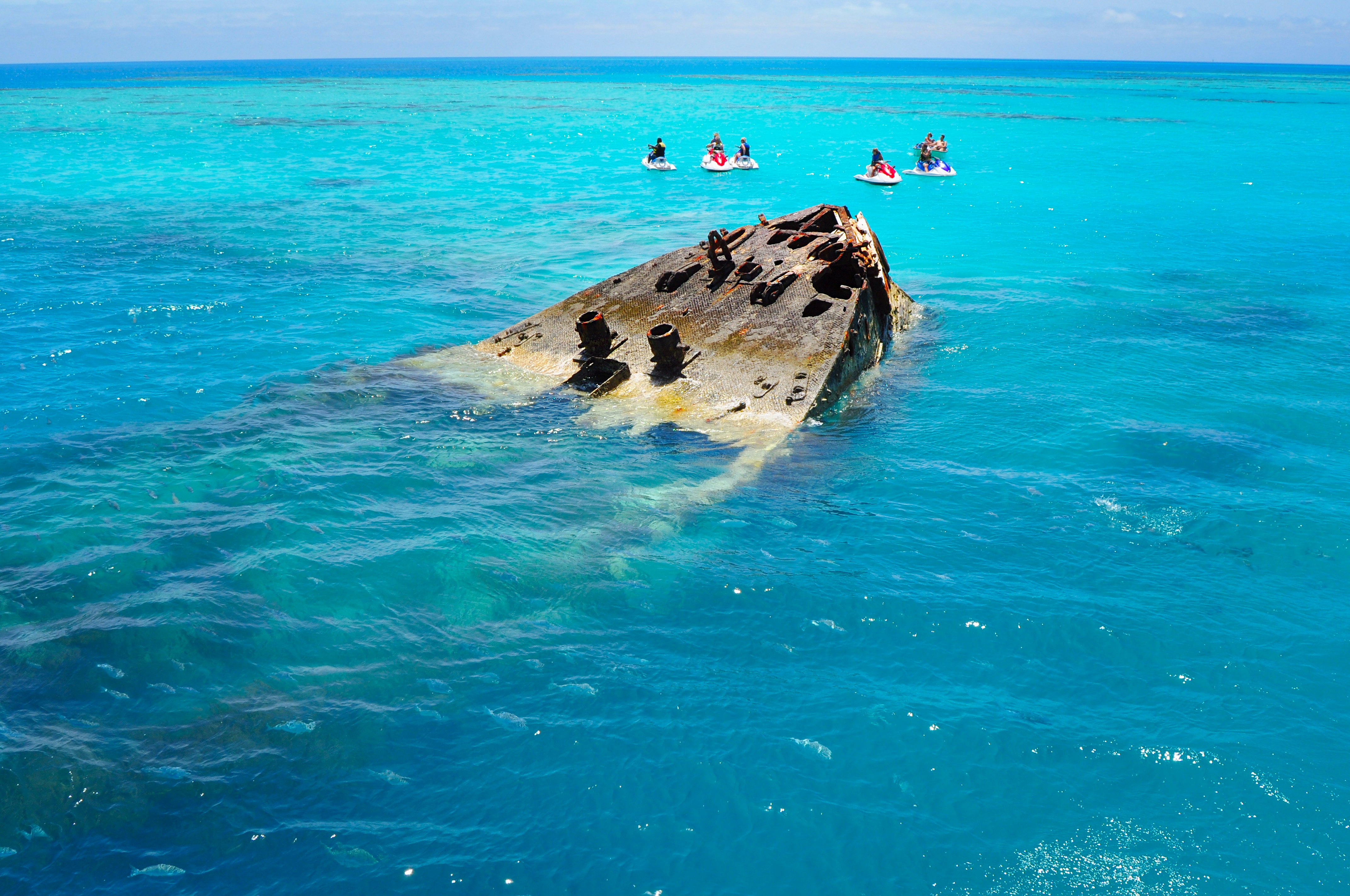 A group of people in jet skis stop next to a semi-submerged shipwreck in ocean near the Bermuda island. 