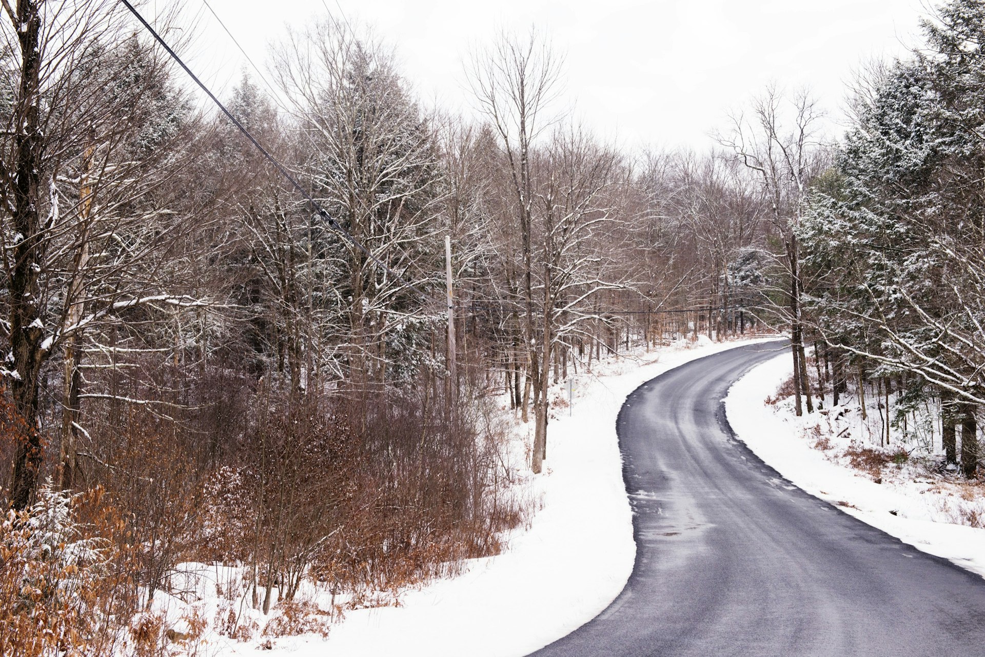 A winding country road in the Catskills mountains. The edges of the paved road are covered in snow. 