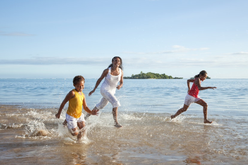 A mother and two kids run along the beach while laughing together in Fiji