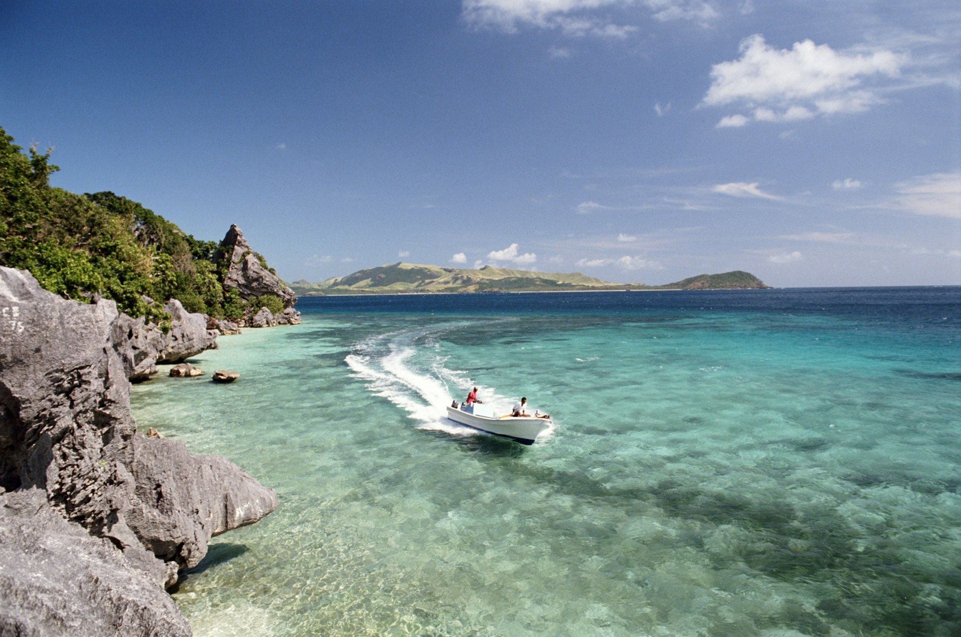 A speedboat cruises through the shallows near an island