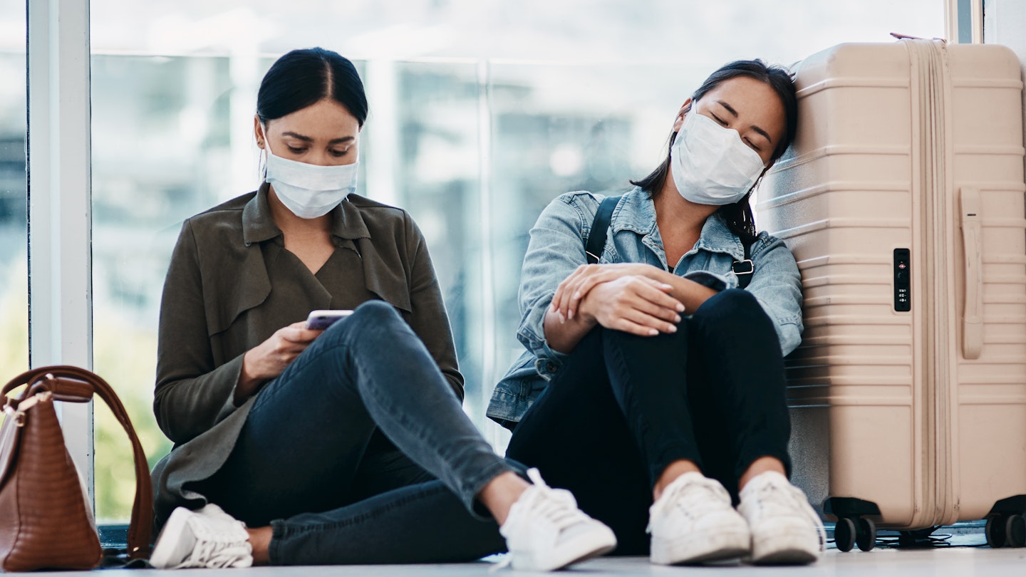 Shot of two young women wearing masks while waiting together in an airport