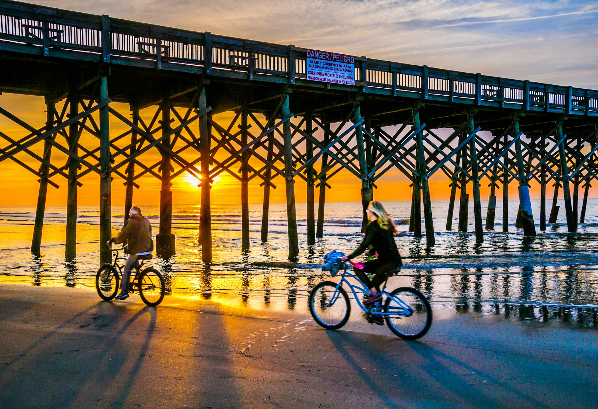 A mature couple ride their bicycles beneath Folly Beach Pier, South Carolina
