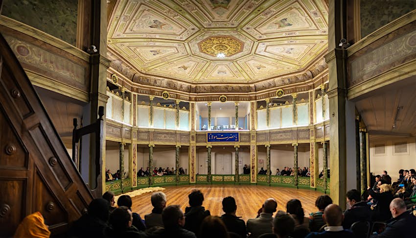 Tourists seated facing an empty round floor at the Galata Mevlevi House Museum