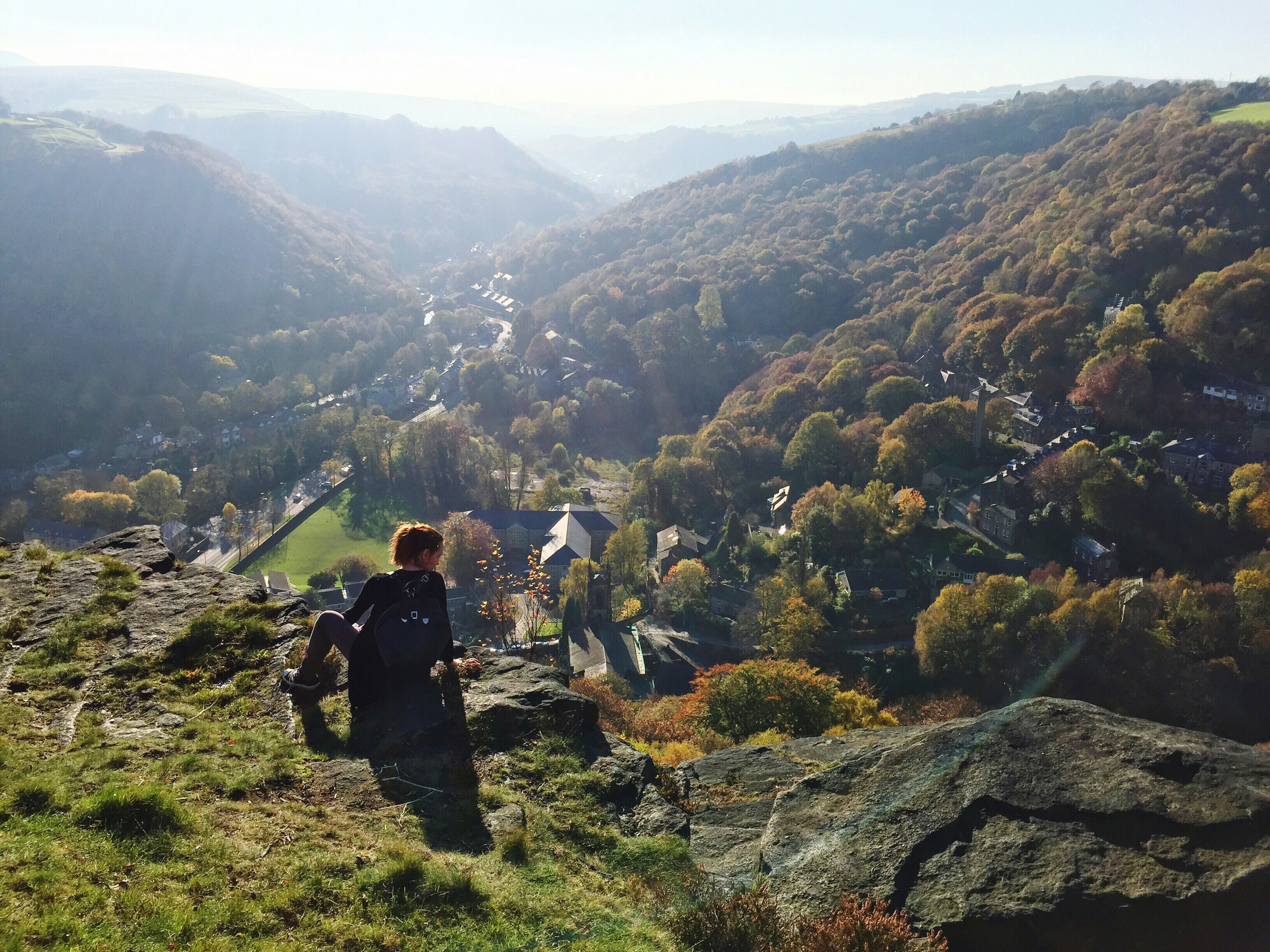 Woman sits on a mountaintop on a sunny day looking over Hebden Bridge, England