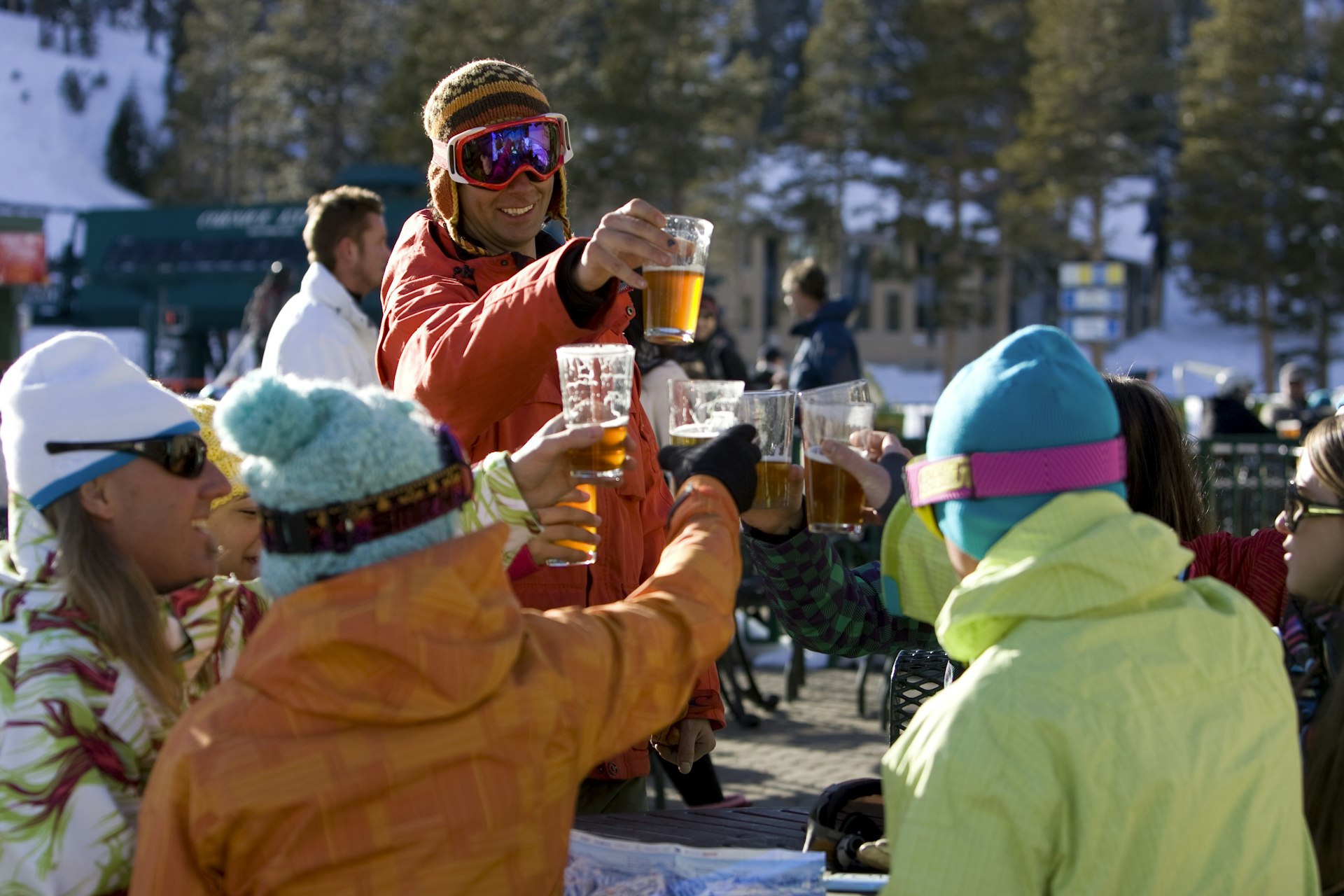 Friends in ski gear socialize and enjoy a beer on the deck on a sunny day on the mountain.