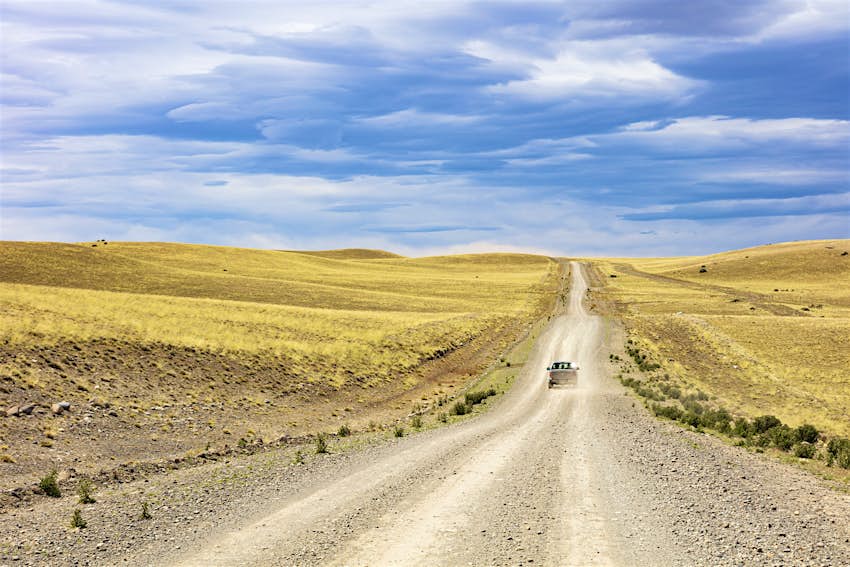 A car drives on a remote gravel road running through grassland
