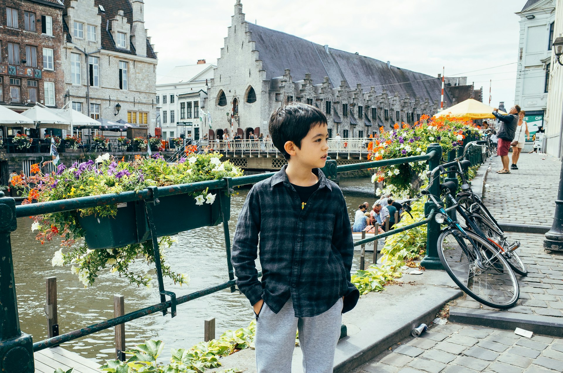 A young boy stands next to a canal in a city with medieval buildings around him