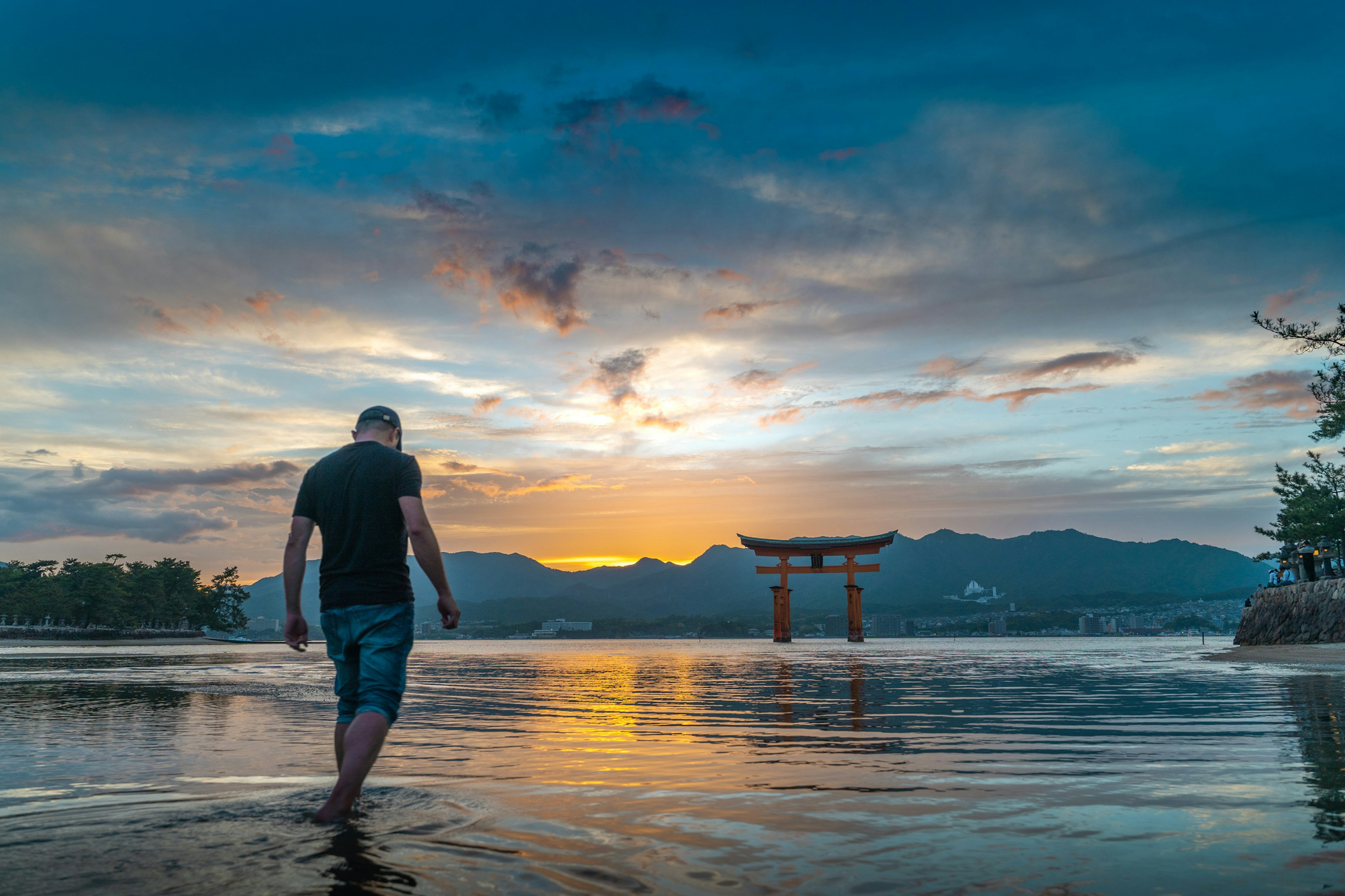 A tourist walks on the sea with the Itsukushima Shrine Torii gate in the back during sunset