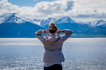 Woman putting on her hood while looking at snowcapped mountains near Anchorage, Alaska.